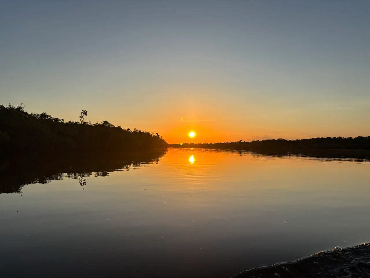 Zonsondergang boven een zijrivier van de Amazone met spiegelglad water