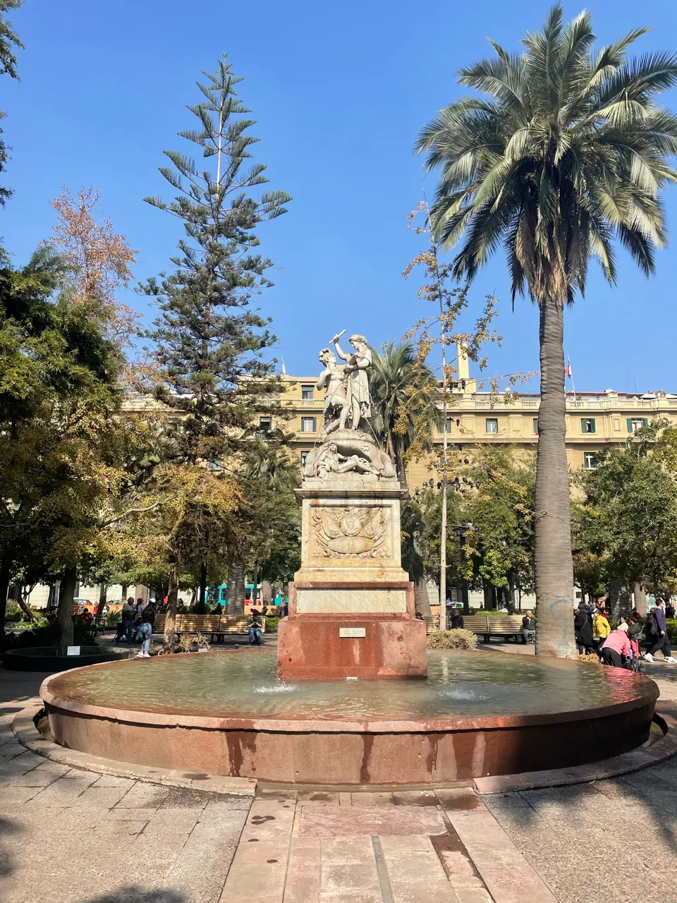 Fontein en standbeeld met palmbomen op het Plaza de Armas in Santiago