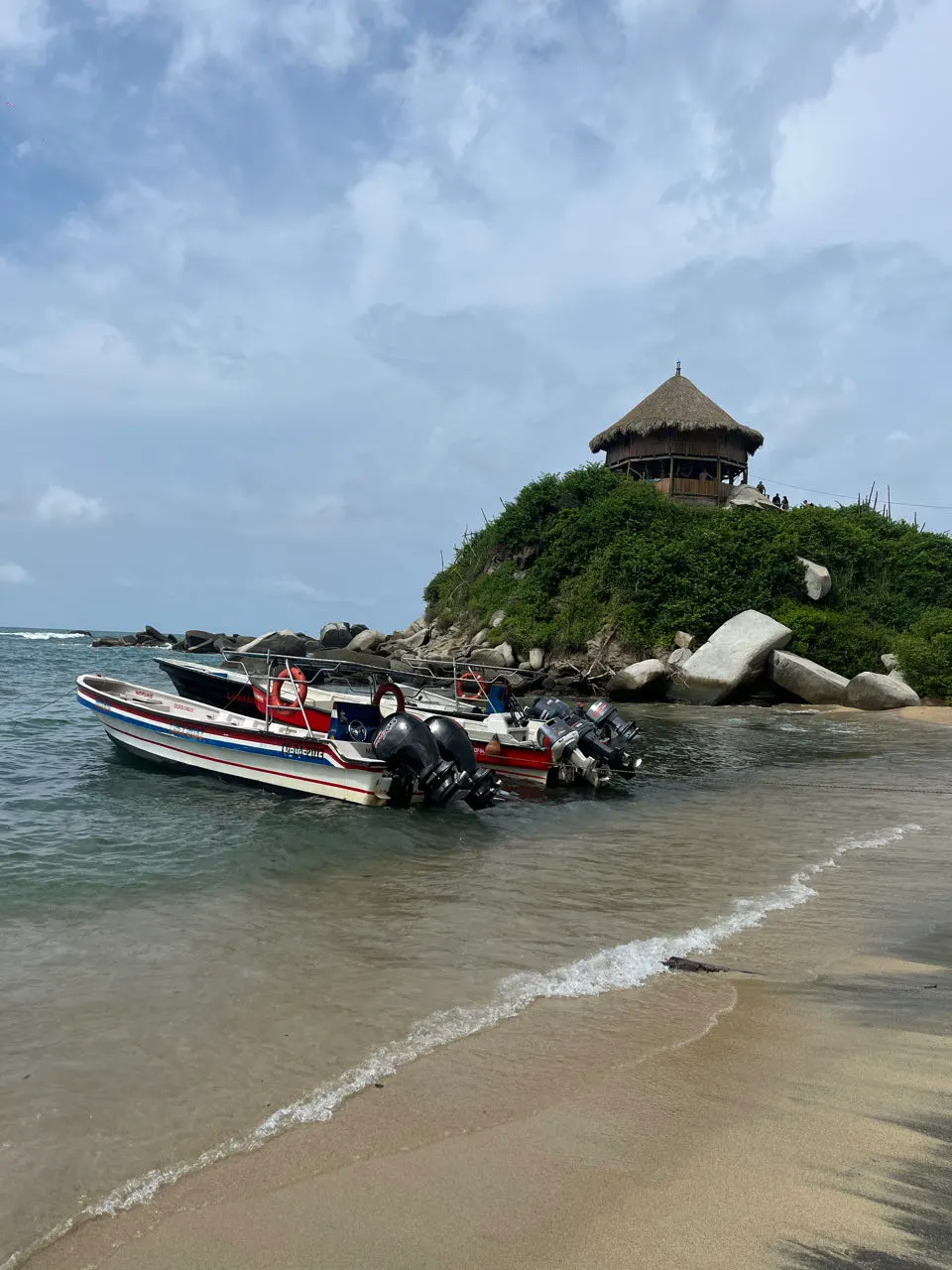 Het uitkijkpunt op een rots bij een strand met bootjes in park Tayrona