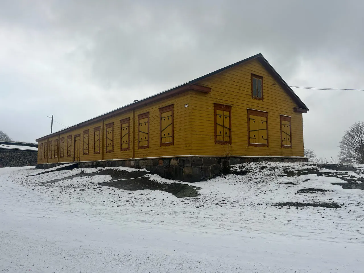 Een lang geel houten gebouw in de sneeuw op Suomenlinna