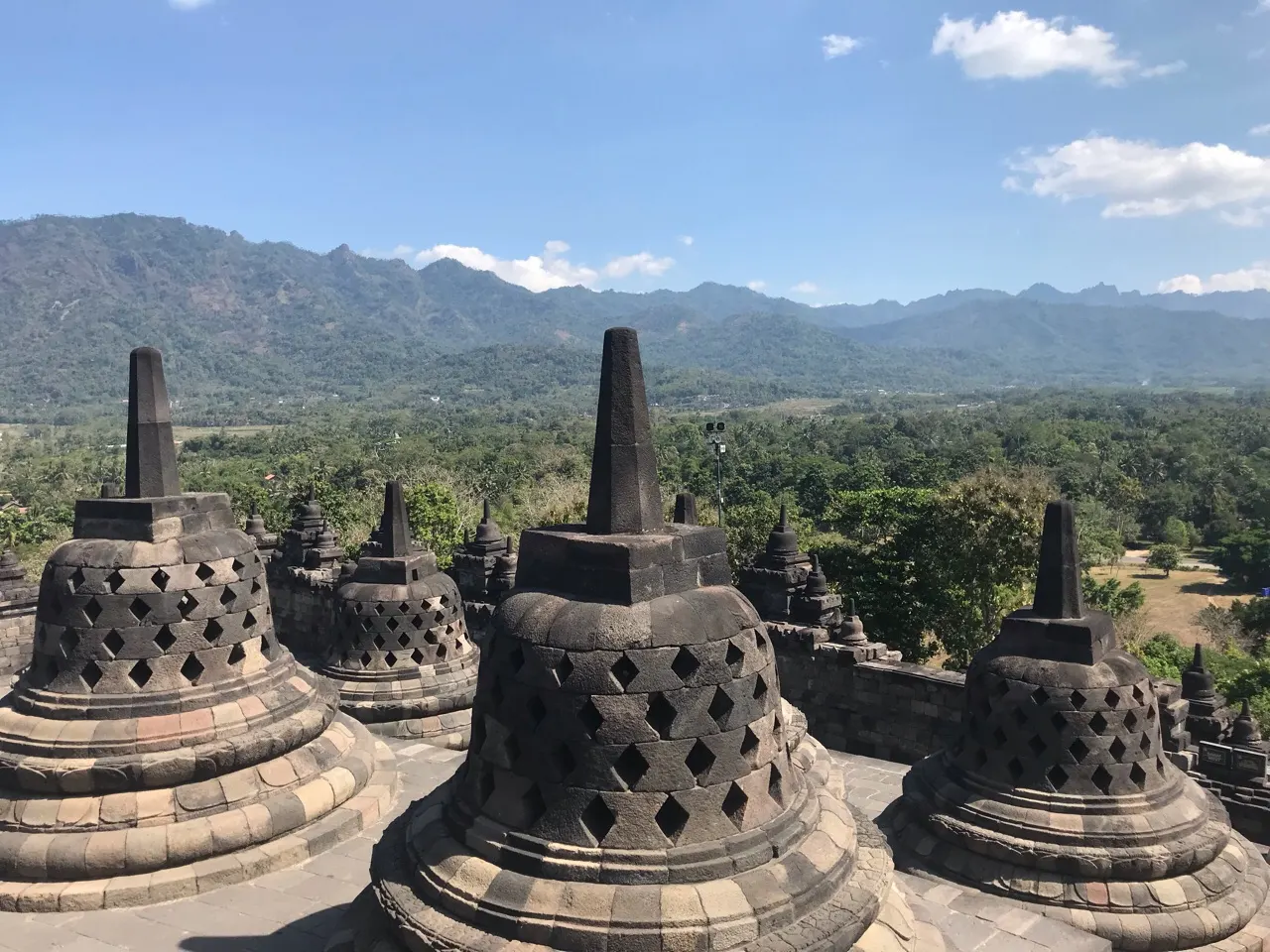 De klokvormige stupa's van de Borobudur met vulkanen en groen op de achtergrond