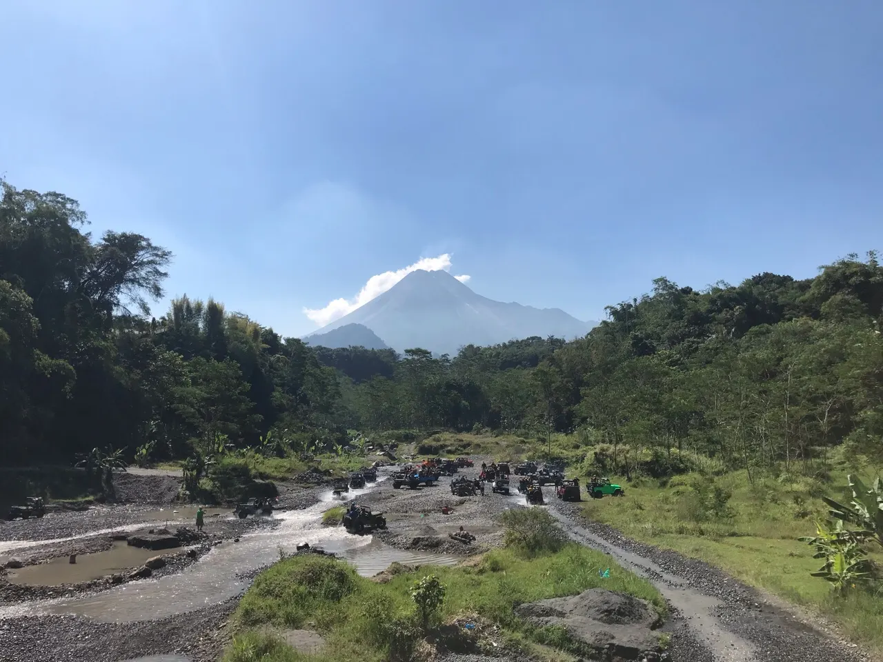 Een breed rivierdal met de rokende top van de Merapi op de achtergrond