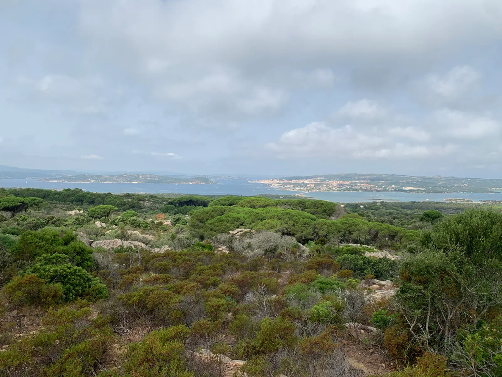 Een witte oude Fiat 500 geparkeerd bij een turquoise baai op Sardinië
