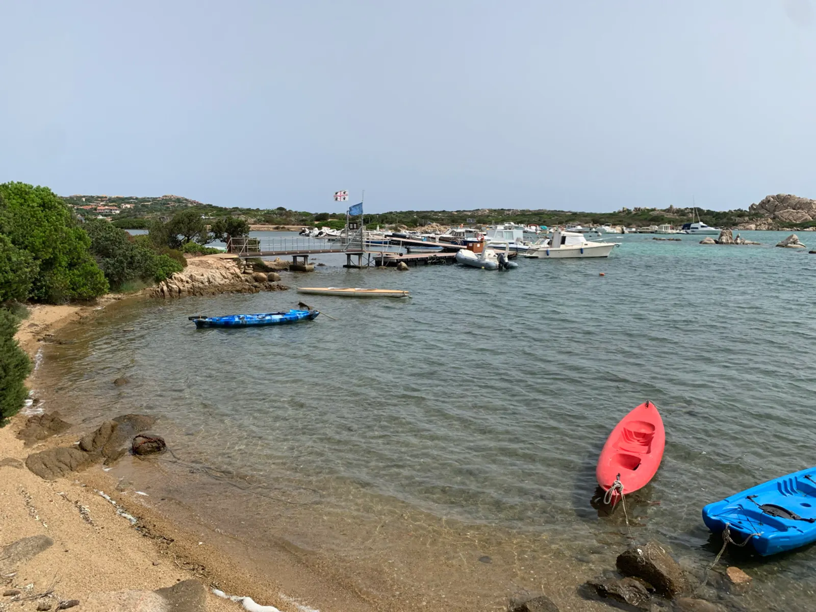 Een strandje met een rode en blauwe kajak op La Maddalena