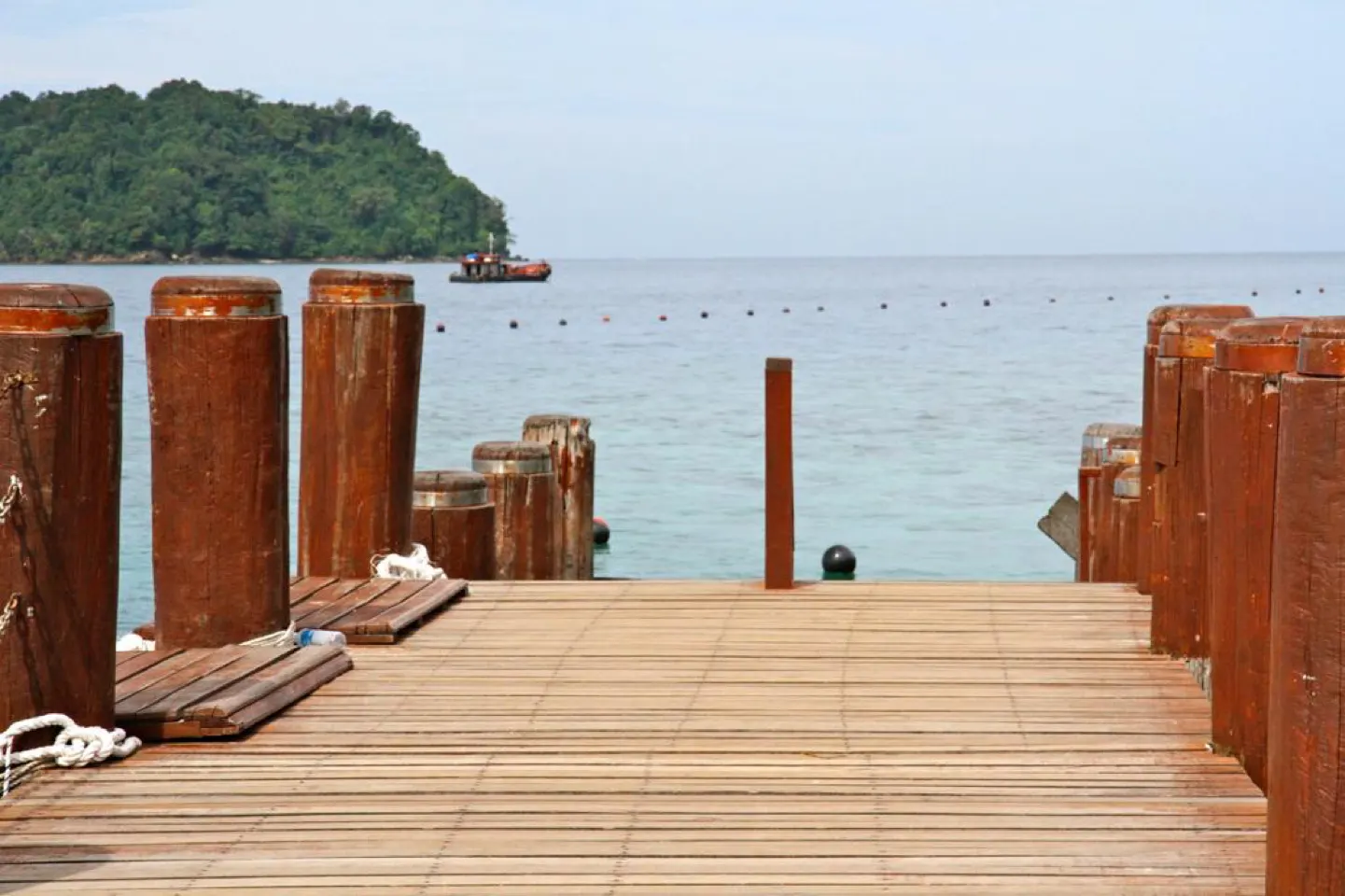 Houten pier die uitloopt over de kalme, heldere zee van een eiland in Sabah