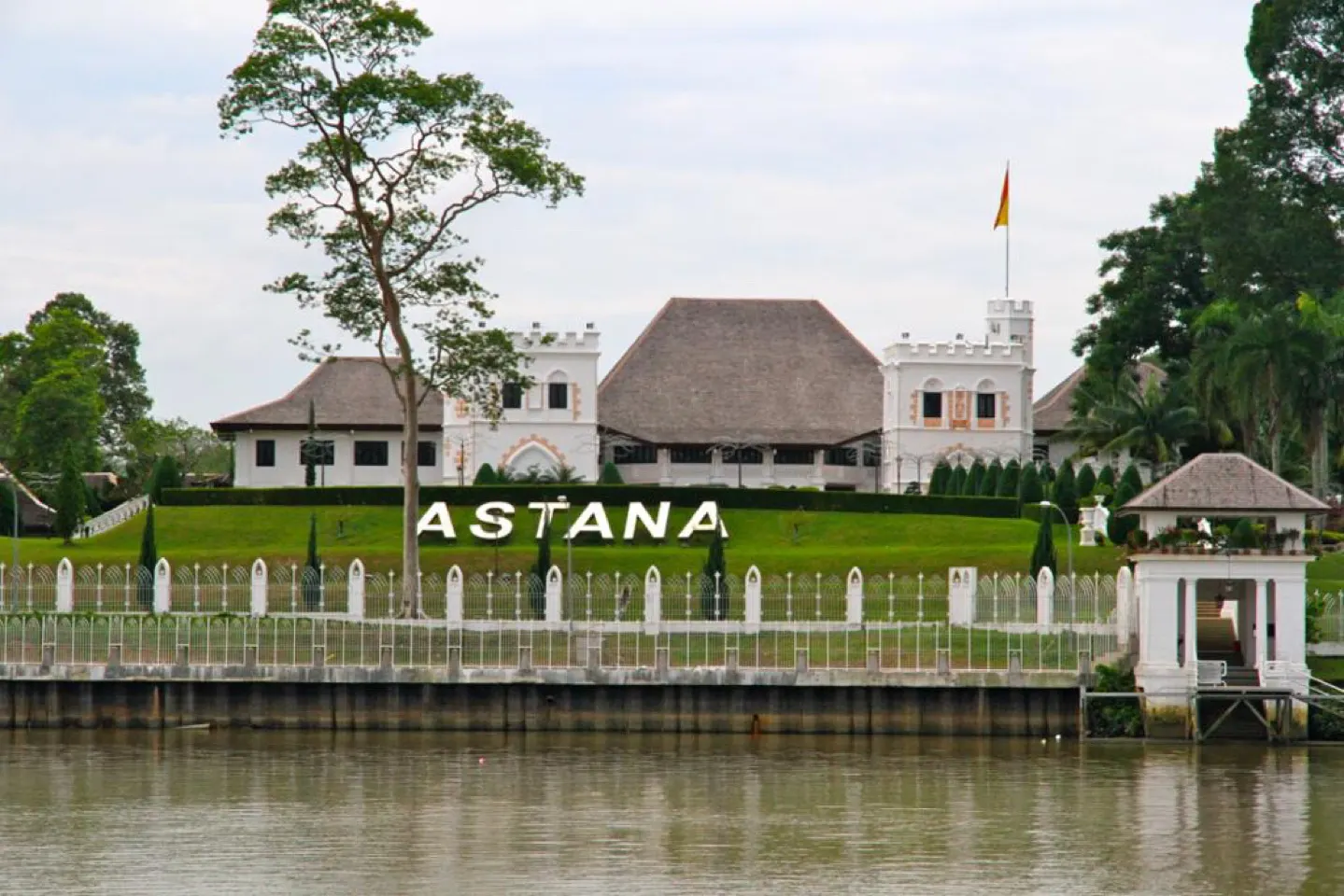 Het witte Astana-paleis met palmbomen aan de overkant van de rivier in Kuching