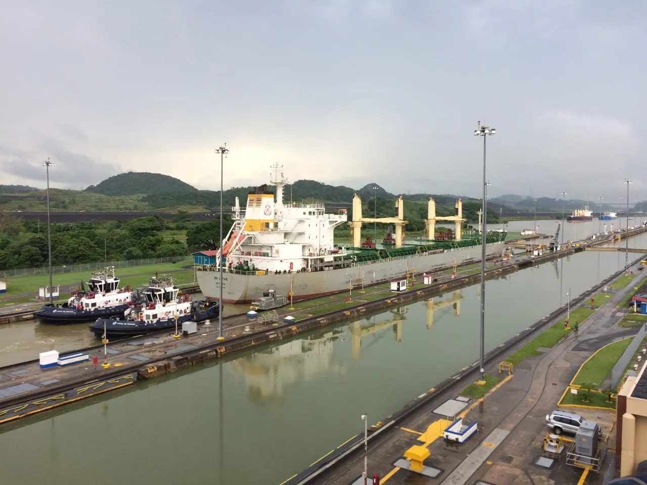 Vrachtschip met een sleepboot in het Panamakanaal met groene heuvels erachter
