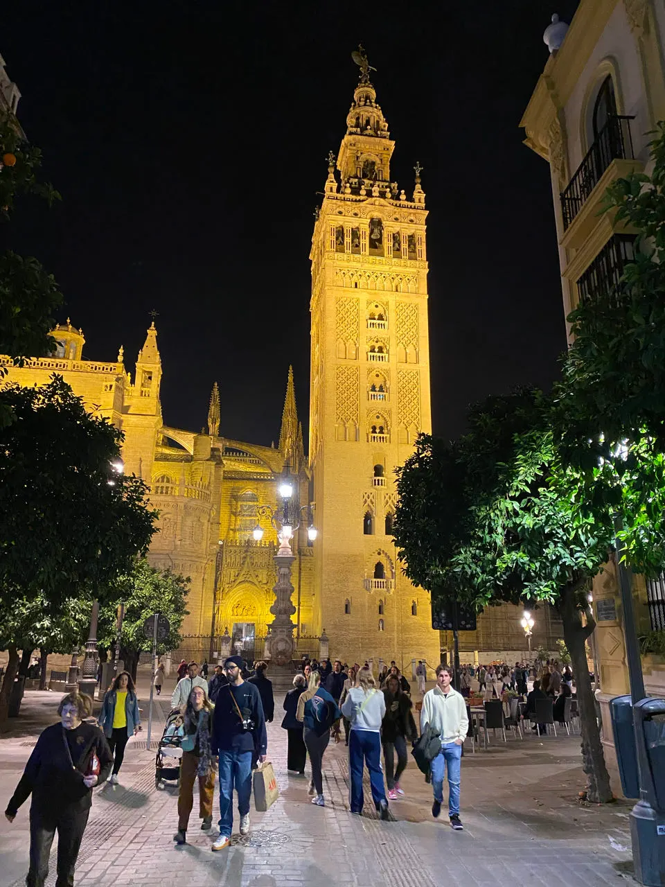 De verlichte Giralda en kathedraal van Sevilla in de avond met mensen op straat